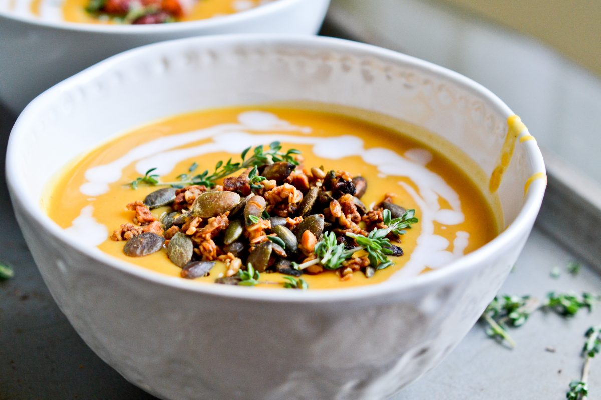 a healthy bowl of pumpkin soup topped with pumpkin seeds and other herbs